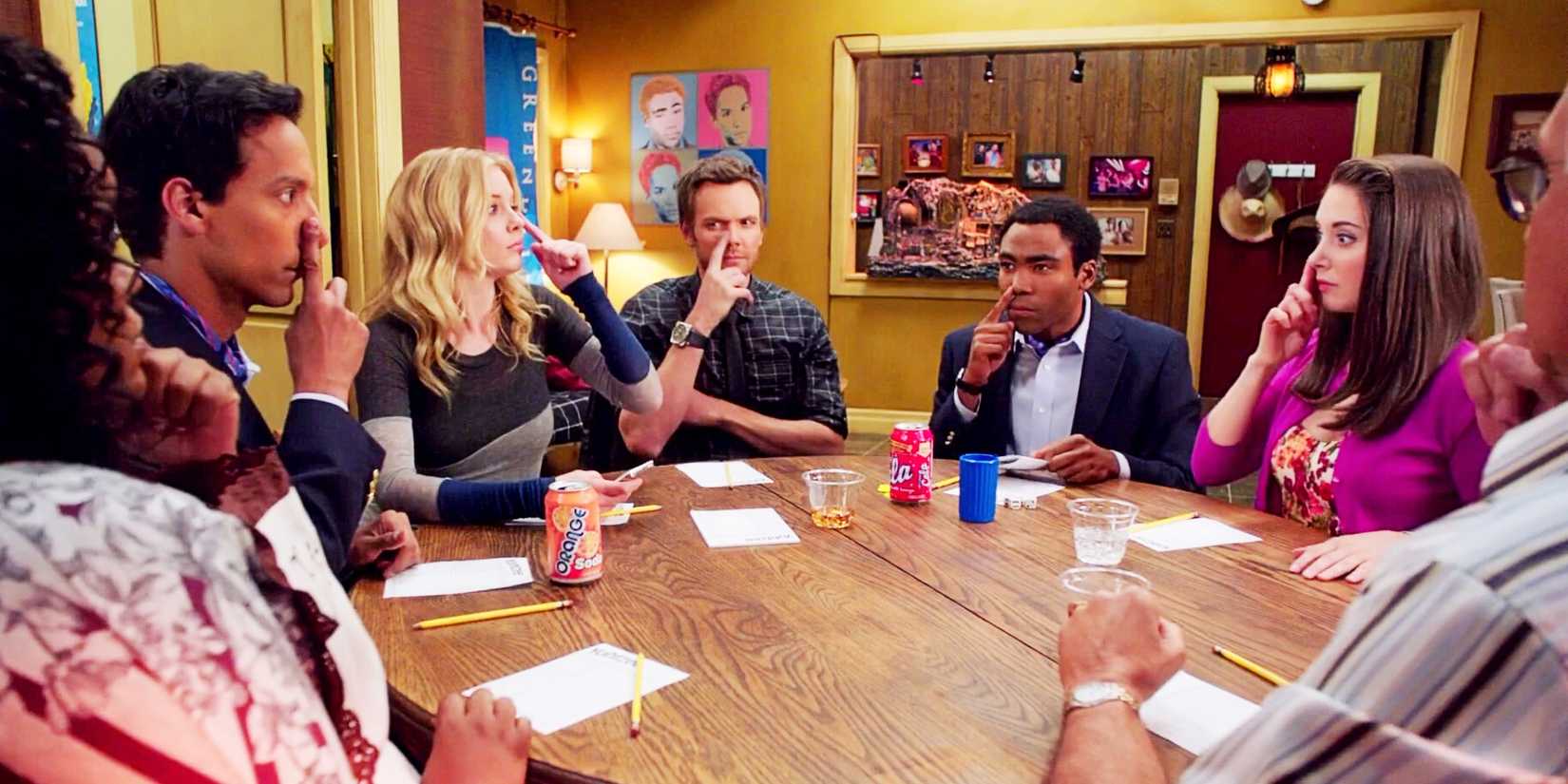 The cast sitting around a table with their fingers on their noses in Community "Remedial Chaos Theory".