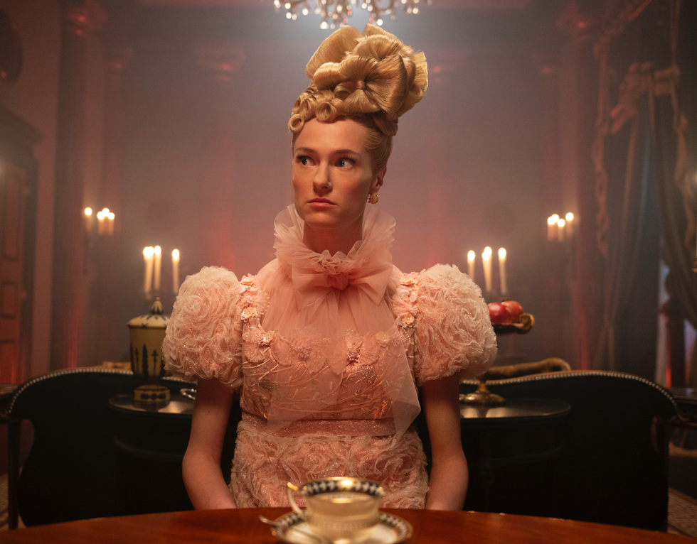 a person seated at a table dressed in a pink vintagestyle outfit with decorative elements