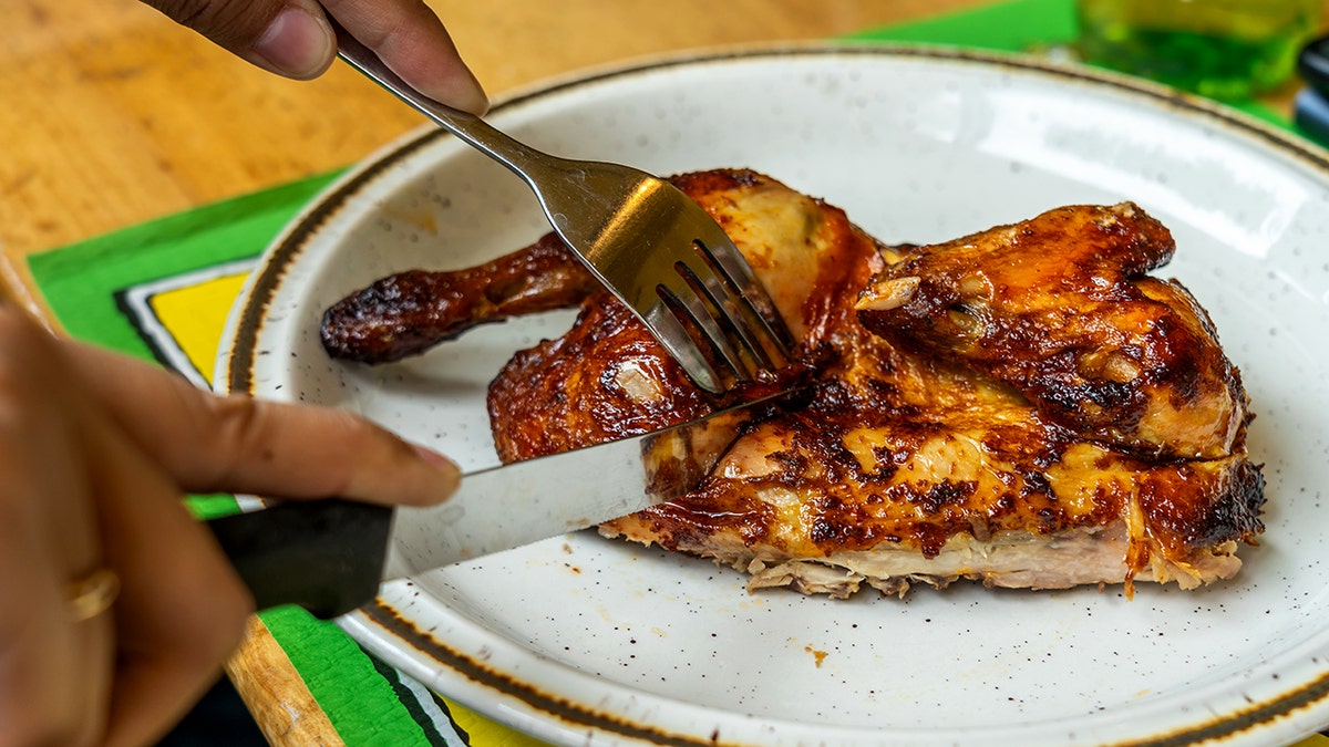 A knife and fork are used to cut into grilled chicken on a plate.