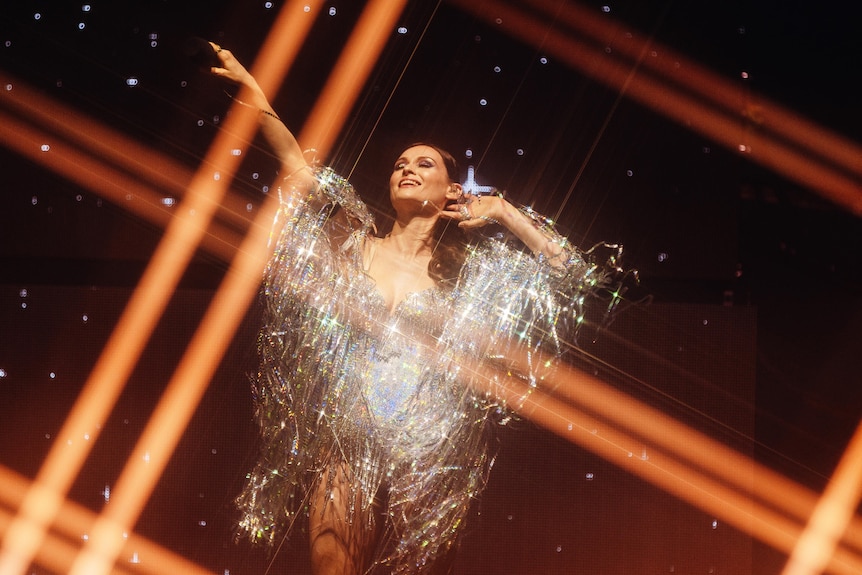Sophie Ellis-Bextor performing & posing in silver tasseled dress, cross-thatched beams of light surround her