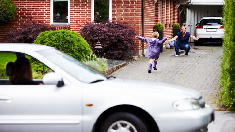 A mother watches from the car as her child hugs the child's father.