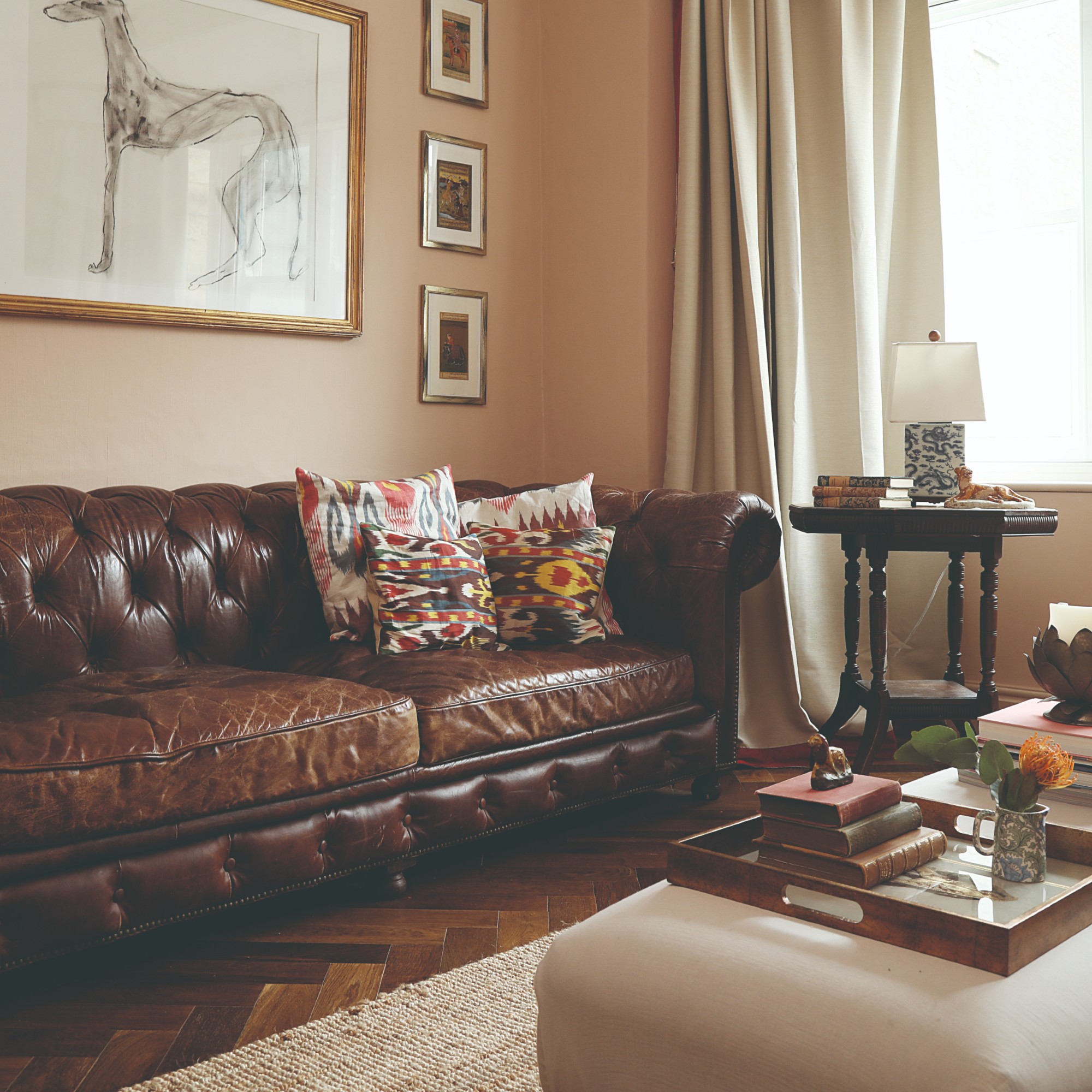 A soft, earthy pink-painted living room with a brown leather Chesterfield sofa