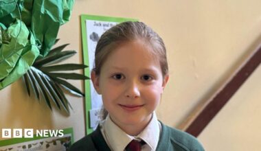 Child is smiling at camera, she is in her school hallway.