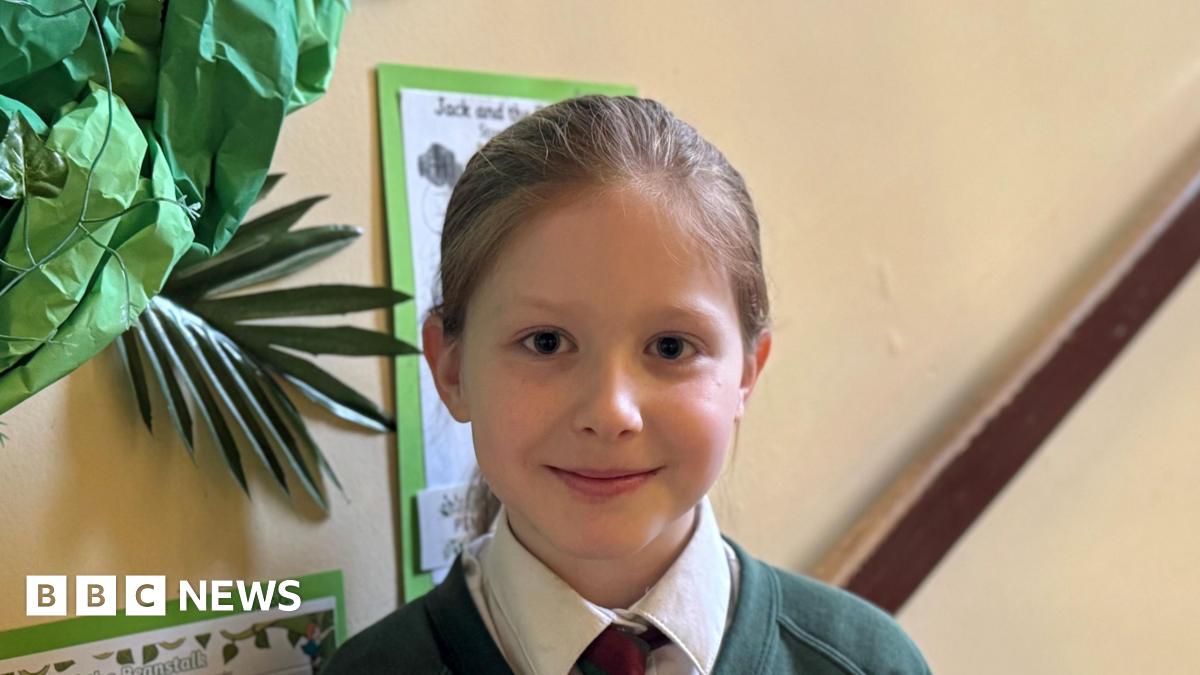 Child is smiling at camera, she is in her school hallway.