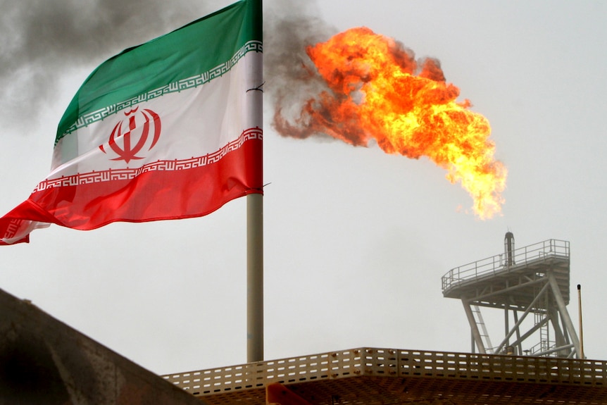 A gas flare on an oil production platform is seen alongside an Iranian flag in the Gulf