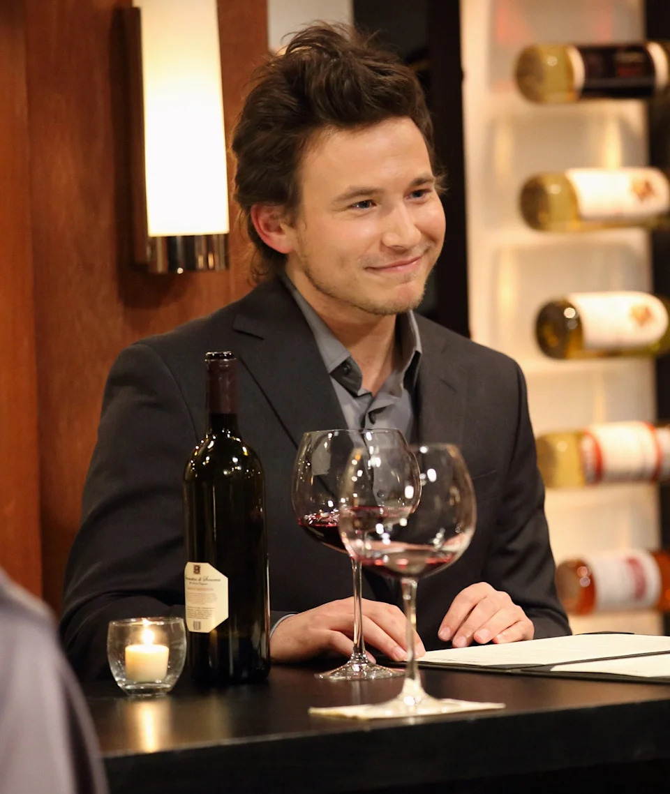 Jonathan Taylor Thomas sitting at a table with wine glasses and a bottle of wine
