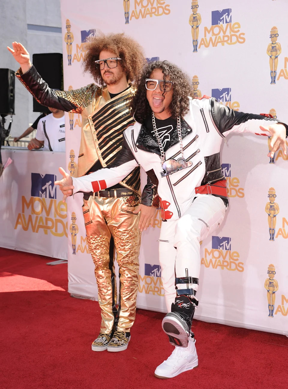 LMFAO pose energetically on the red carpet at the MTV Movie Awards, wearing vibrant, eclectic outfits with bold patterns and striking accessories