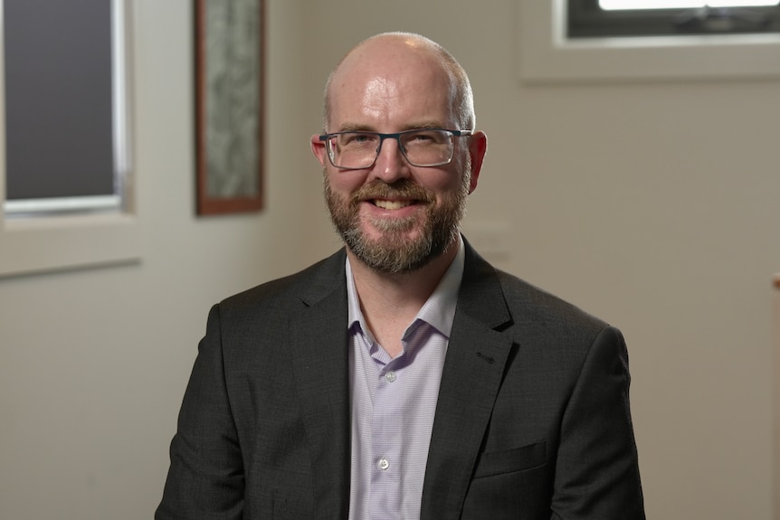 Gerard Burg, wearing a suit, sits in an office, smiling at the camera.