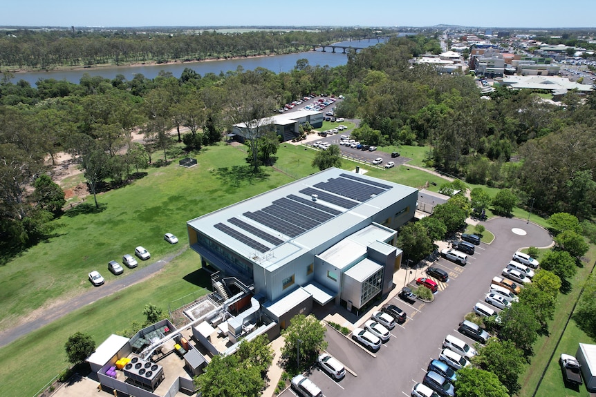 A drone shot of the top of a hospital building covered with solar panels, a river and bridge in the background