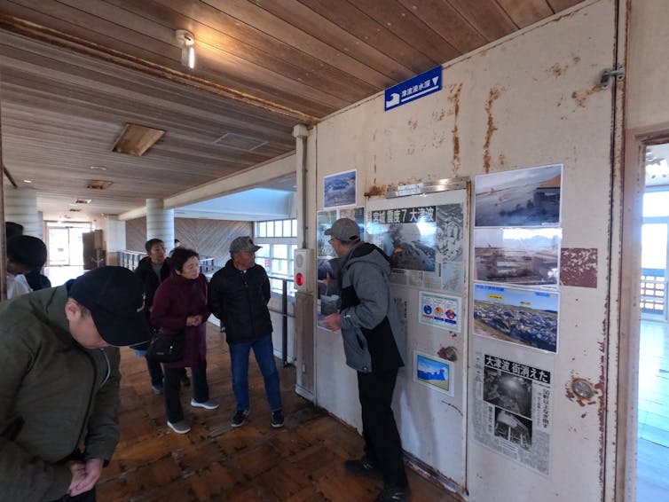 a man points to images on a wall while speaking to a group of people.