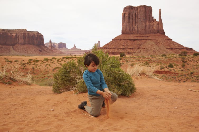 A child plays with sand in in front of a rock formation in Monument Valley