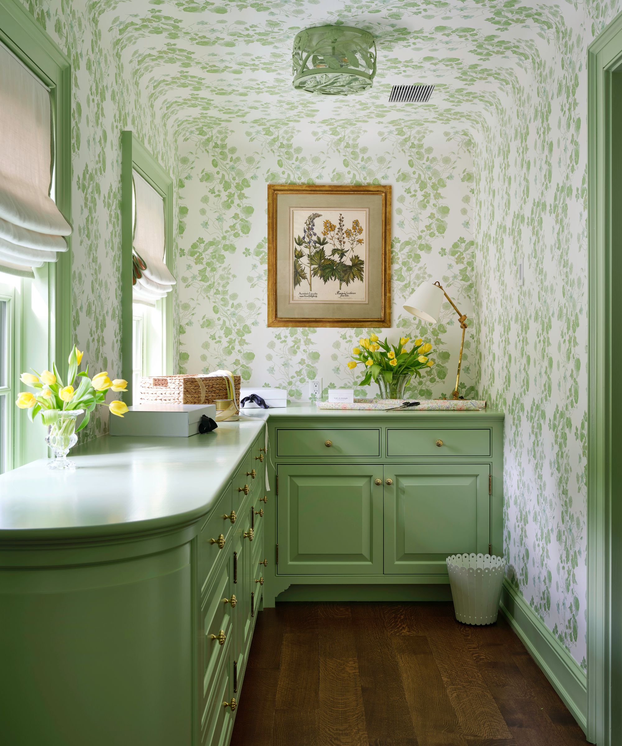 Pale green home office with painted cabinetry, floral wallpaper, a vintage botanical framed picture and vases of tulips