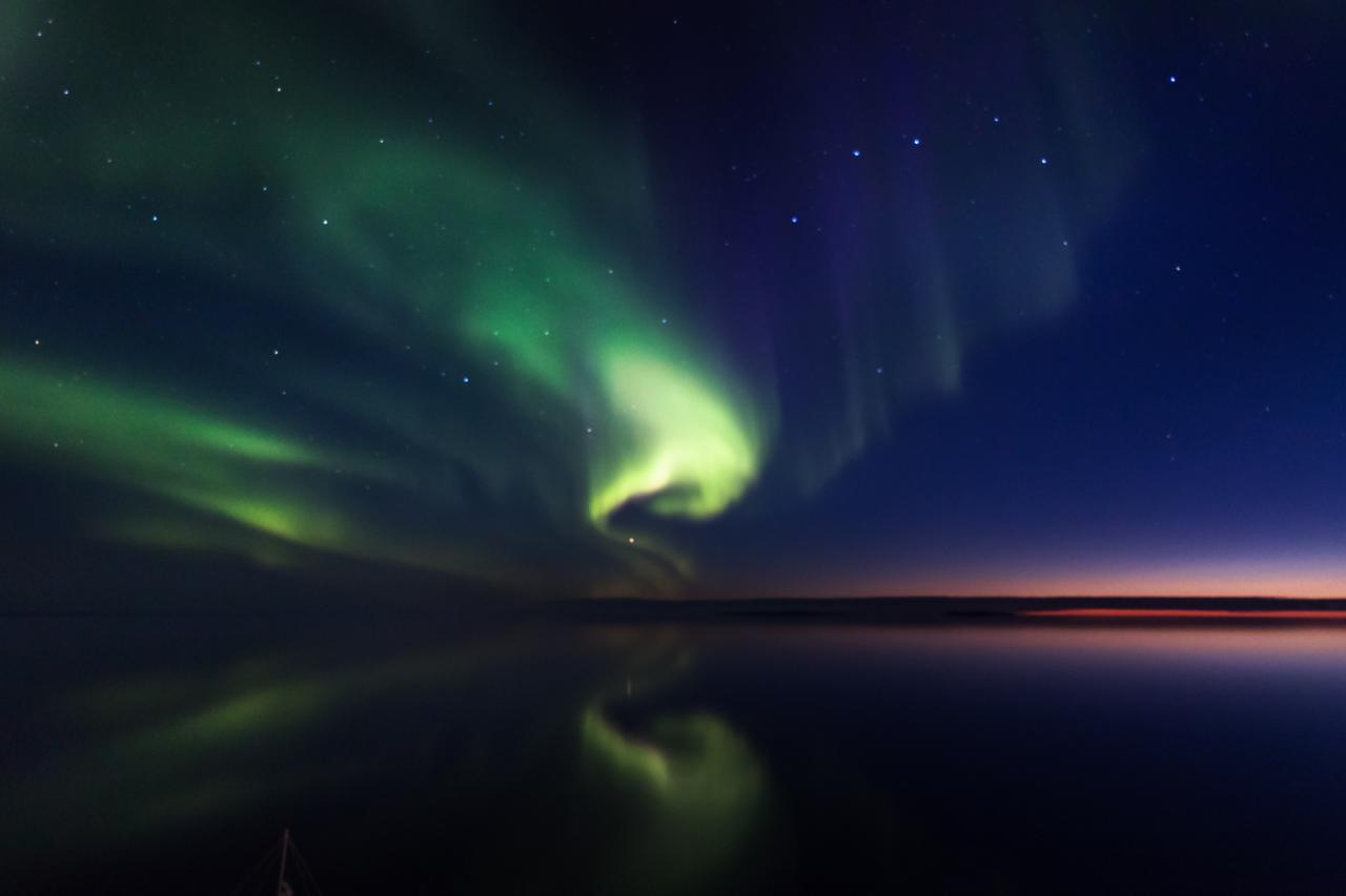 The aurora borealis, or northern lights, illuminates the night sky and reflects off a calm body of water. (Adobe Stock Photo)