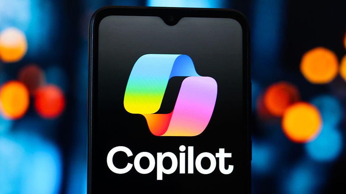 Copilot logo on a black smartphone in front of blue background with multicolored dots.