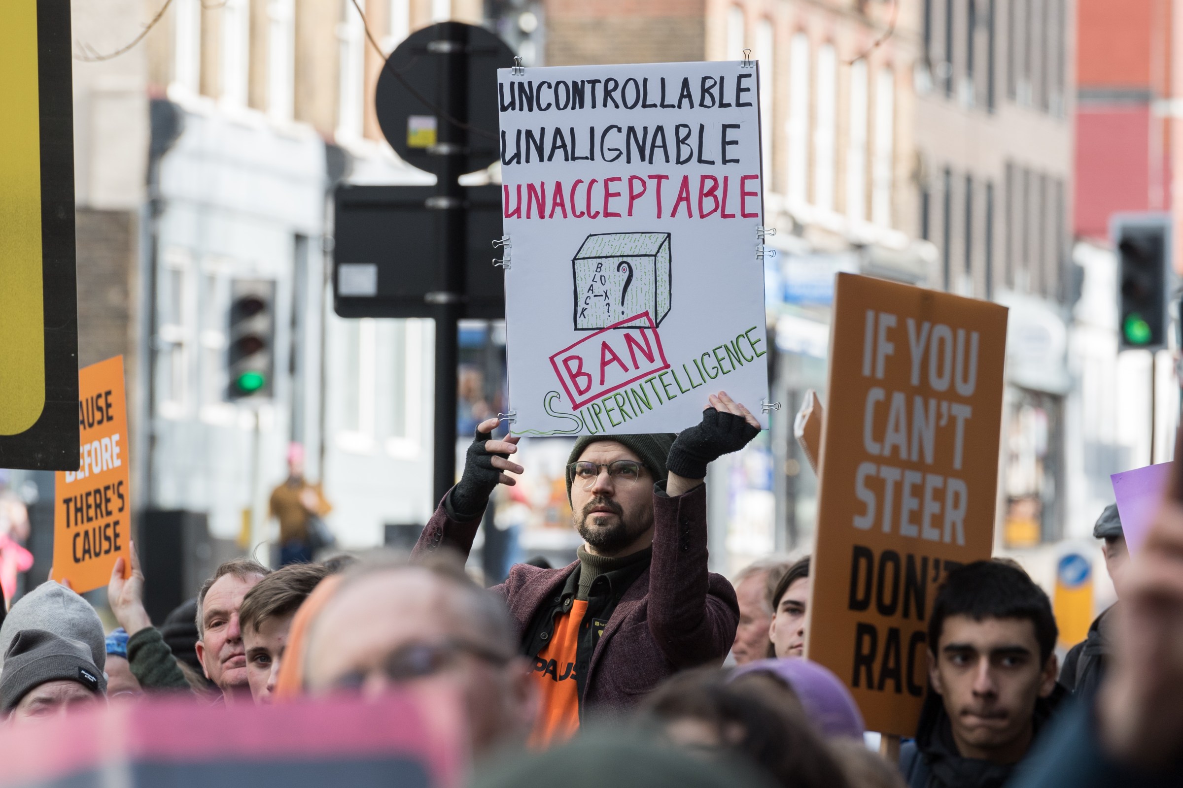 A man holds up an anti-AI sign at a protest outside of OpenAI’s headquarters. The sign says uncontrollable, unalignable, unacceptable. Ban superintelligence.
