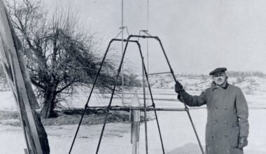 On a snowy March 16, 1926, Dr. Robert H. Goddard rests his hand on the testing frame supporting his liquid fuel rocket at Ward Farm in Auburn, Massachusetts. A wooden door is propped up at an angle next to the frame where Goddard’s assistant, Henry Sachs, later sheltered after lighting the rocket.