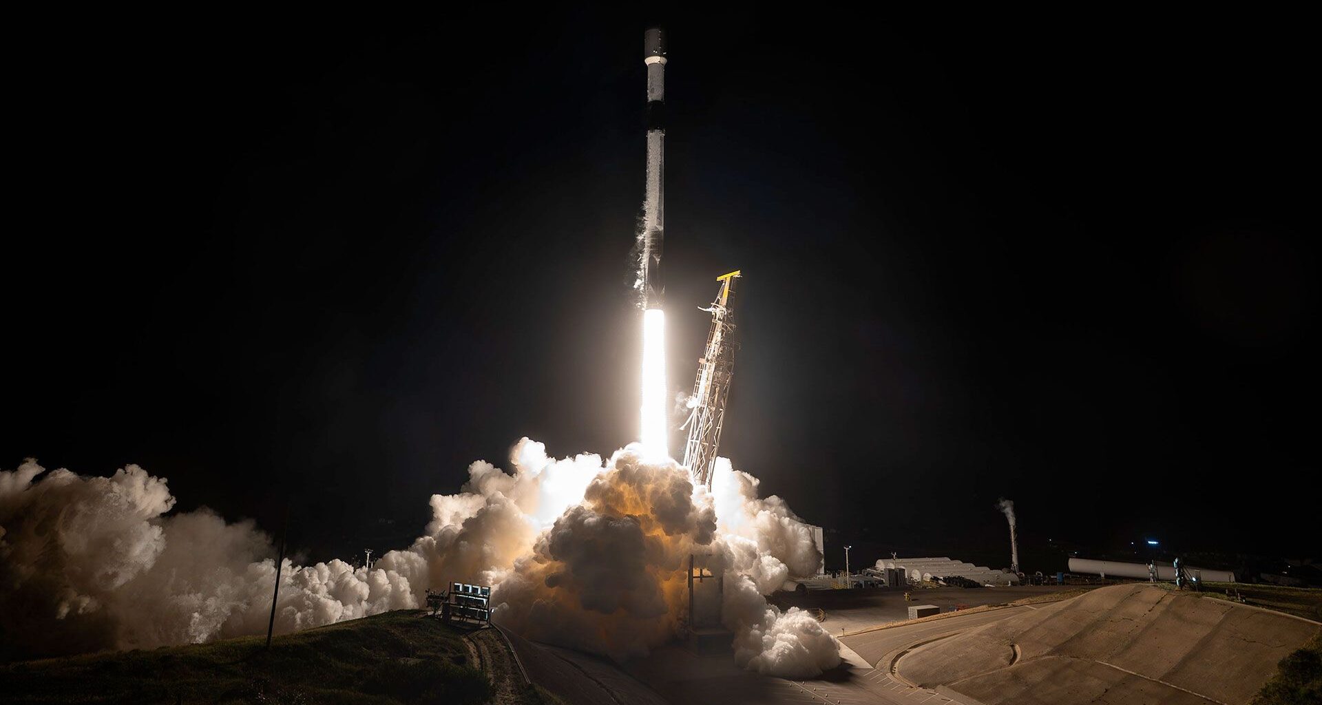 a rocket lifts off into the night sky, lighting up the area around its launch pad