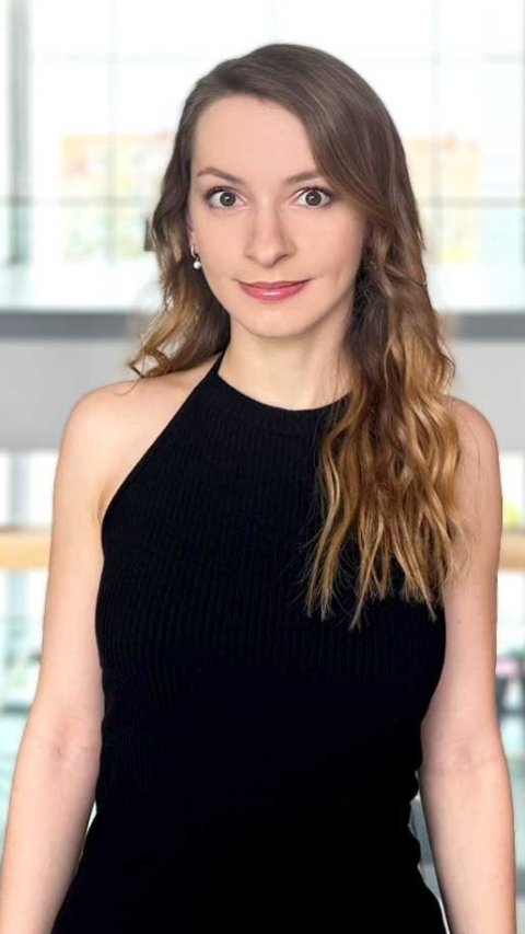 Dr Katarzyna Herbetko is standing in front of a slim wooden railing in the well-lit atrium of a hospital