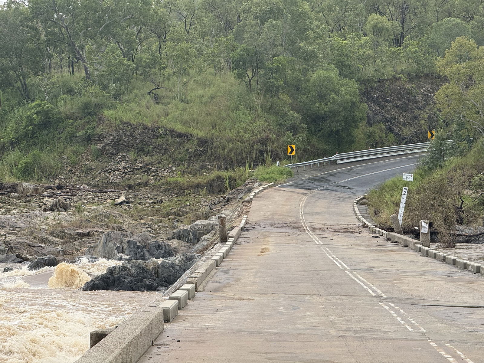 Brown water of a high river laps against the pillars of a road bridge