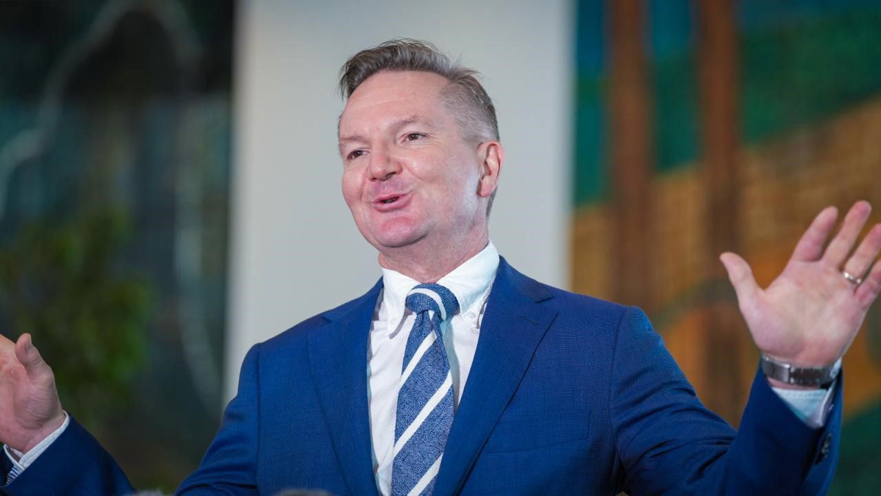 Chris Bowen raises his hands at a press conference and smiles.