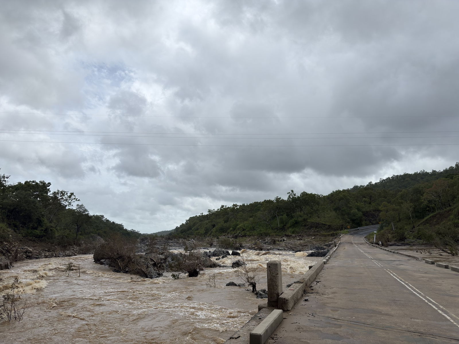 Brown water of a high river laps against the pillars of a road bridge