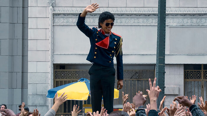 Actor portraying Michael Jackson in the Michael Movie cast waving to a crowd during a street scene.