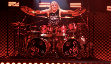 Mikkey Dee playing drums on stage during a live Scorpions concert, with stage lighting and the audience in the background.
