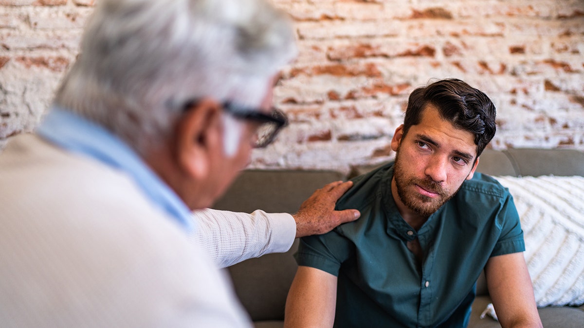 Young patient man talking to psychotherapist during therapy session at clinic
