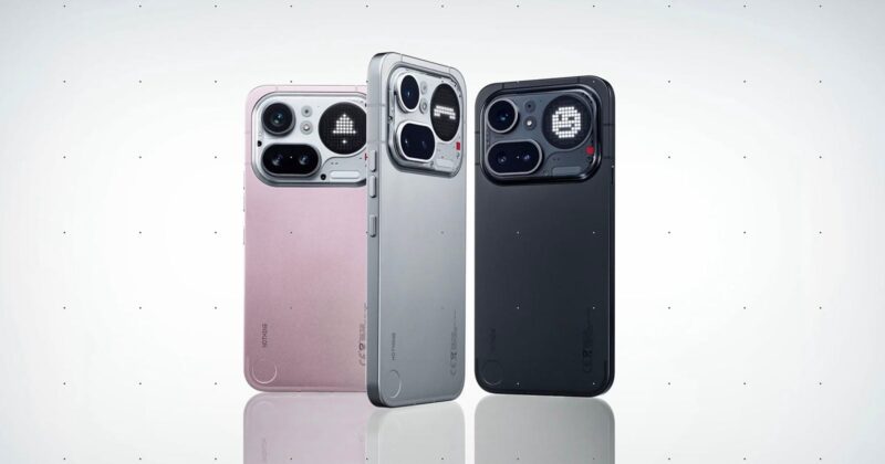 Three smartphones are standing upright side by side, displayed in pink, silver, and black colors. Each phone has a distinctive large camera module with multiple lenses and sensors on a minimalist back design.