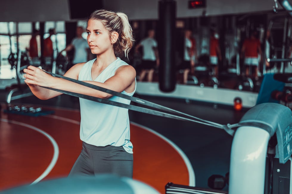 attractive women working out with stretching rubber band in the gym, wearing blue sportswear, side shot