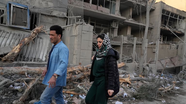 People walk past buildings damaged during a strike on a police station during ongoing, joint U.S.-Israeli military attacks in Tehran, Iran, Monday, March 2, 2026.