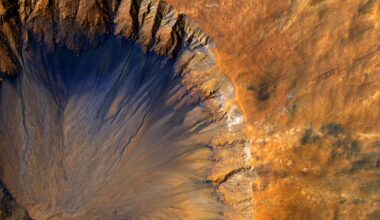 An impact crater with a sharp rim seen from above. Most of the landscape is orange, while the steep inner slope on the north side of the crater is a deep blue-black.