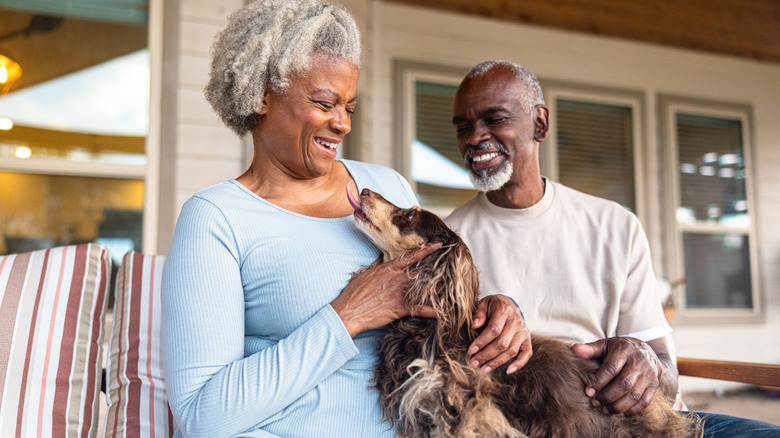 Elderly couple sit outside home while playing with dog