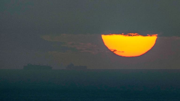  Ships sail through the Arabian Gulf toward the Strait of Hormuz as the sun sets in the United Arab Emirates.