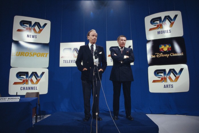 Rupert Murdoch and Andrew Neil at the standing on a stage with various screens in the background showing the logos for Sky TV channels.