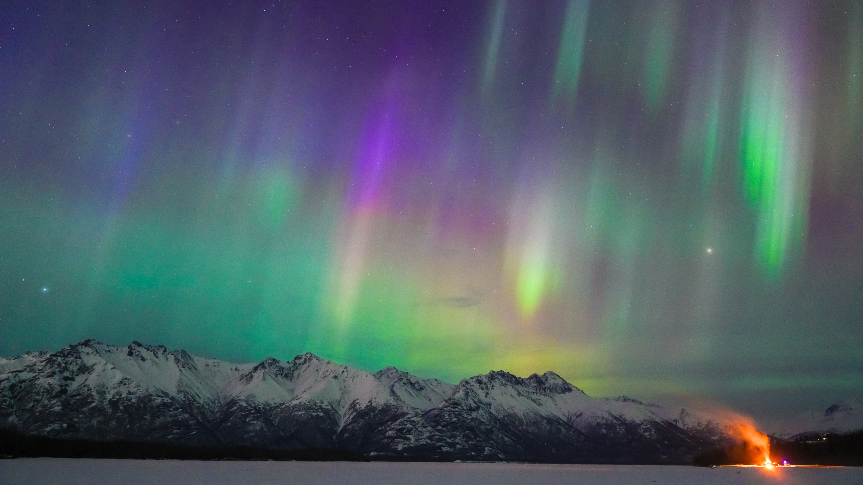 curtains of green and purple aurora stretch across the sky above snowcapped mountains