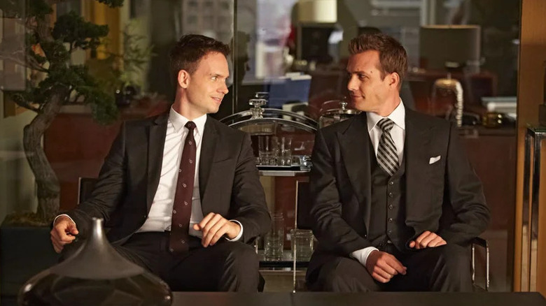 Mike Ross (Patrick J. Adams) and Harvey Specter (Gabriel Macht) smile at each other while seated in an office in Suits