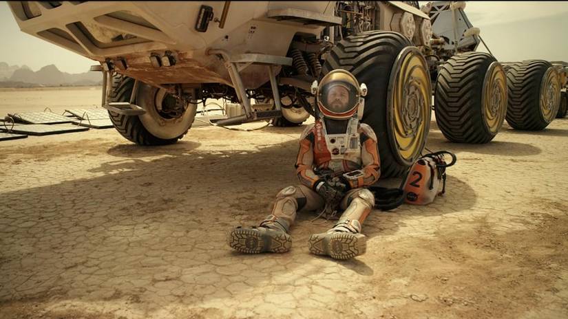 Matt Damon at Mark Watney leans against a Mars rover in the Martian