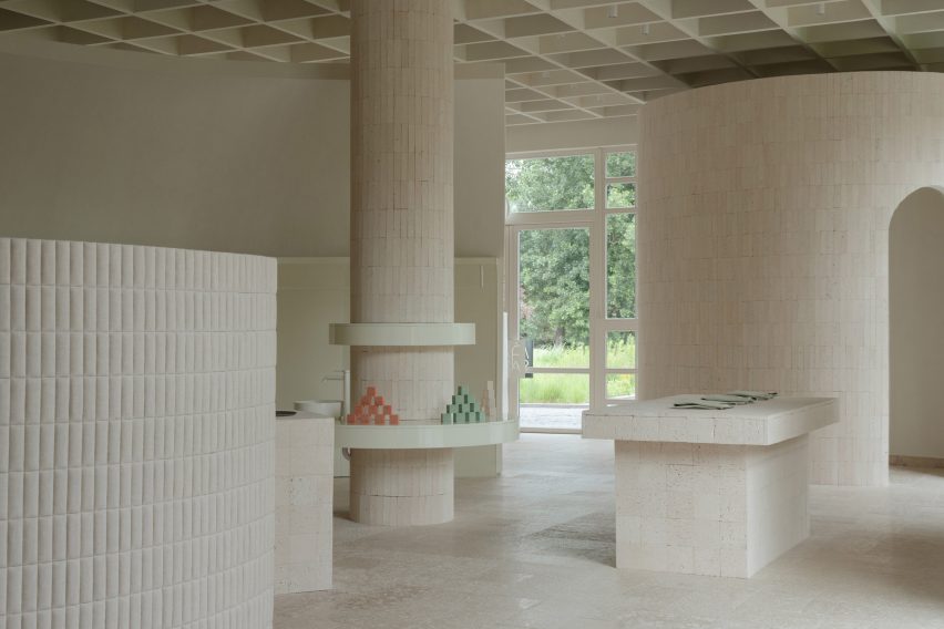 An image of a neutral, cream-toned interior with architectural elements including columns, a cylindrical room and a rectangular table made from travertine and limestone.