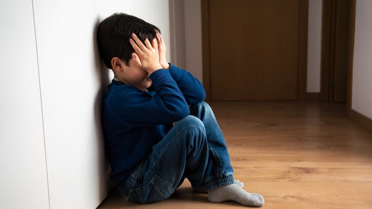 Upset problem child with head in hands sitting on floor.