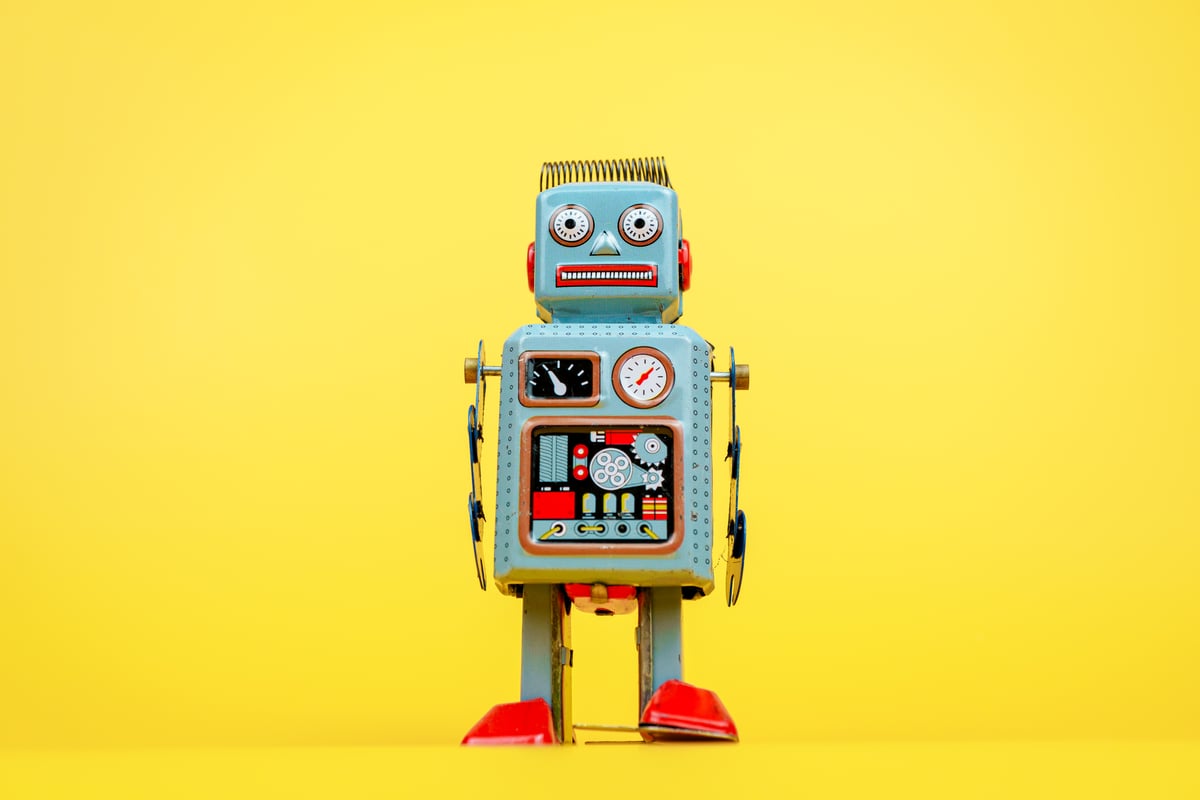 A robot looks at the camera. Yellow background.