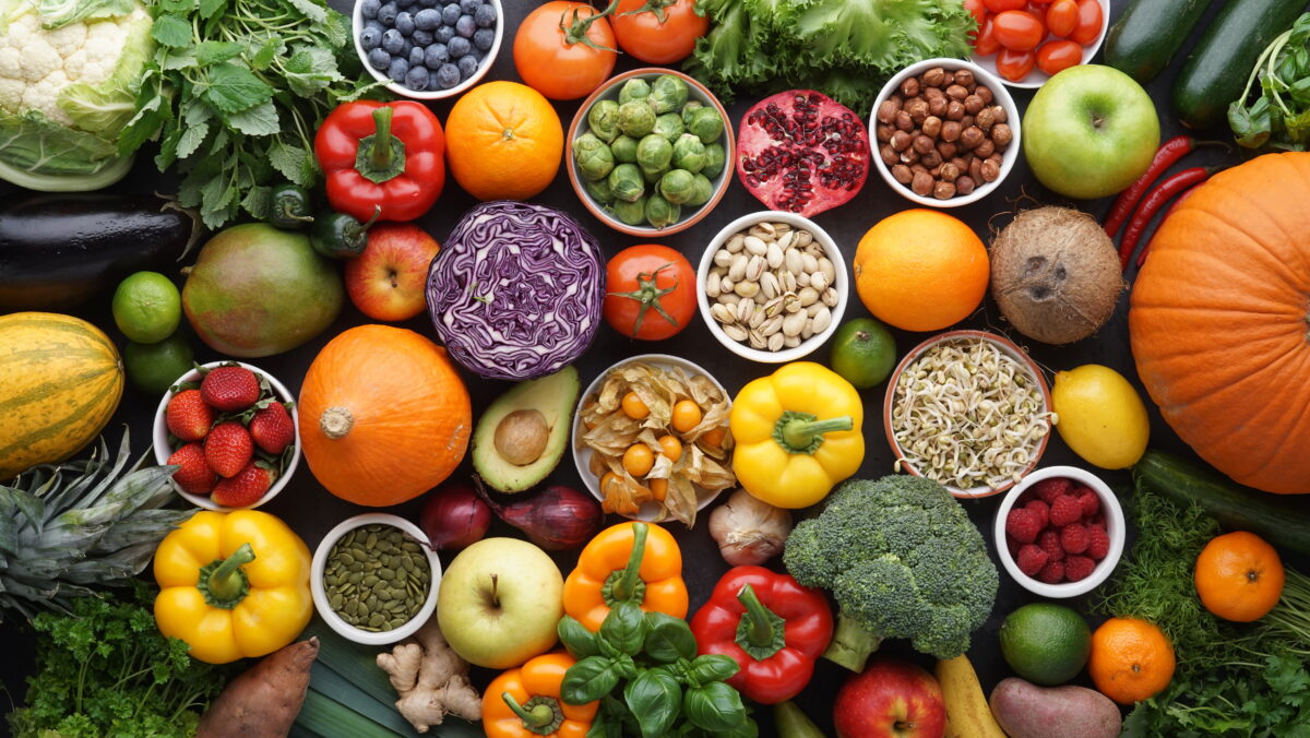 Photo shows a large, colorful spread of fresh fruits, vegetables, nuts, and seeds