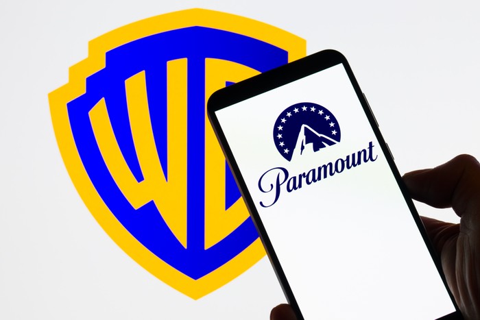The Paramount logo is displayed on a mobile phone with the Warner Bros Discovery icon seen in the background.