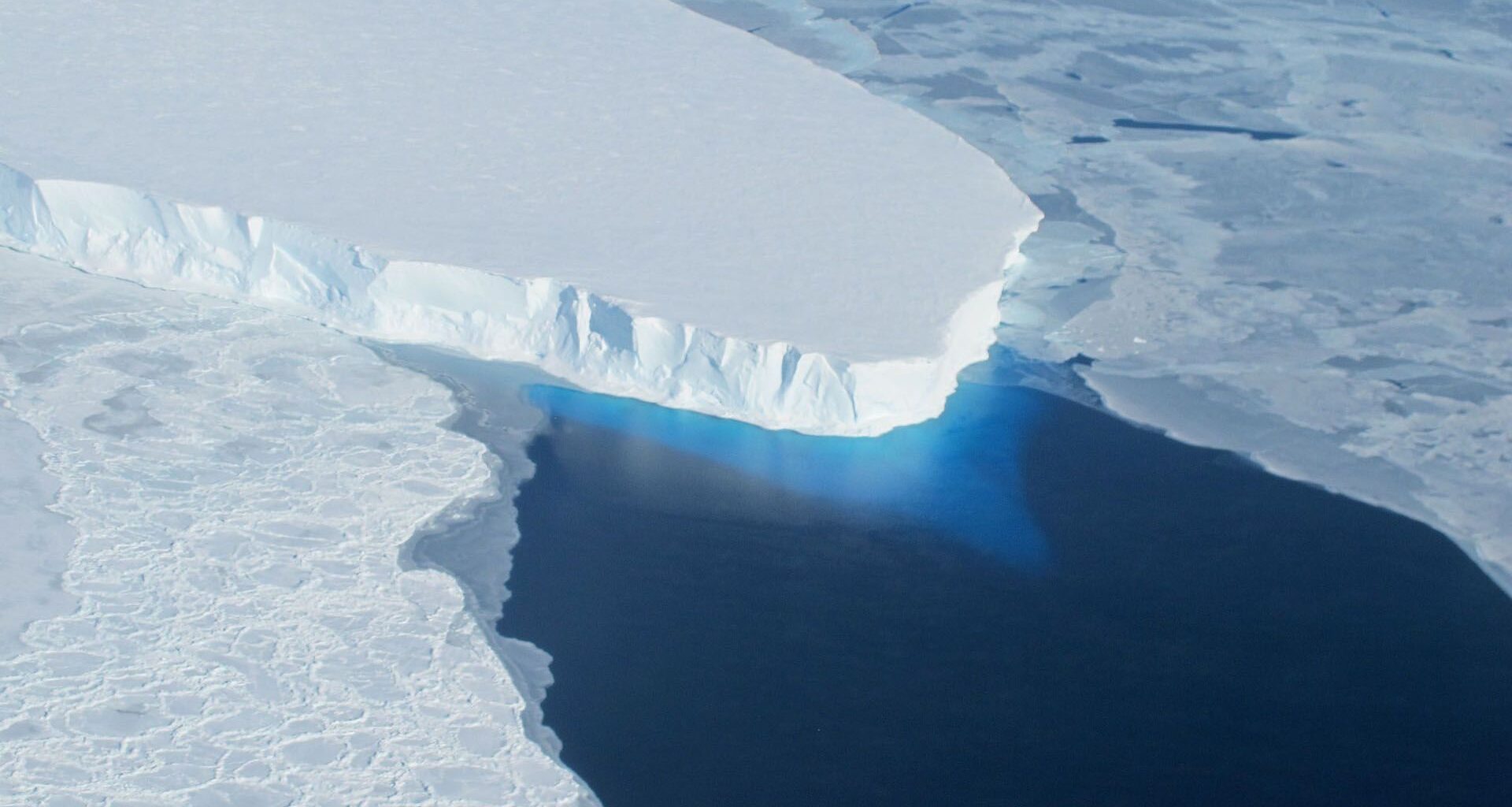 aerial photo of a large glacier, which juts out into a bay of dark-blue seawater