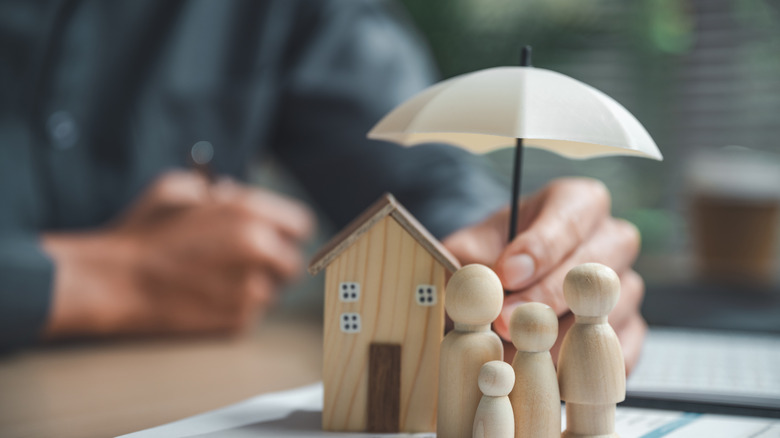 A wooden umbrella held over models of a home and family to symbolize financial security.