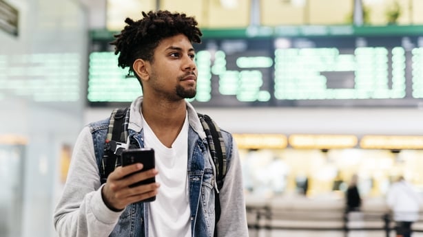 Young man inside the airport holding a mobile phone.young afro man holding a mobile phone looking at the departures of planes in an airport