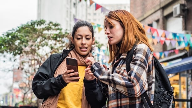 Young woman showing something on mobile phone to her friend in the city