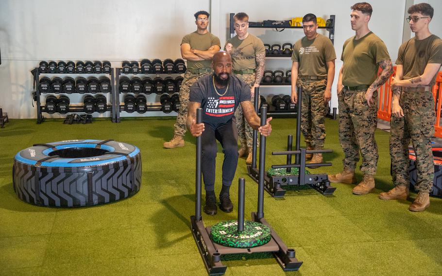 A man pushes a weighted sled as U.S. Marines watch during a fitness training session inside a gym.