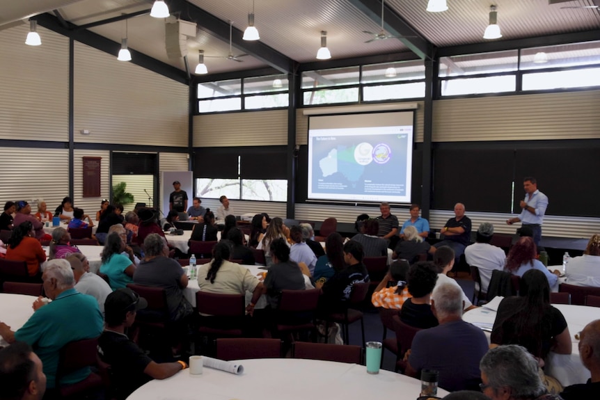 Man stands in front of a room of people speaking into a microphone.