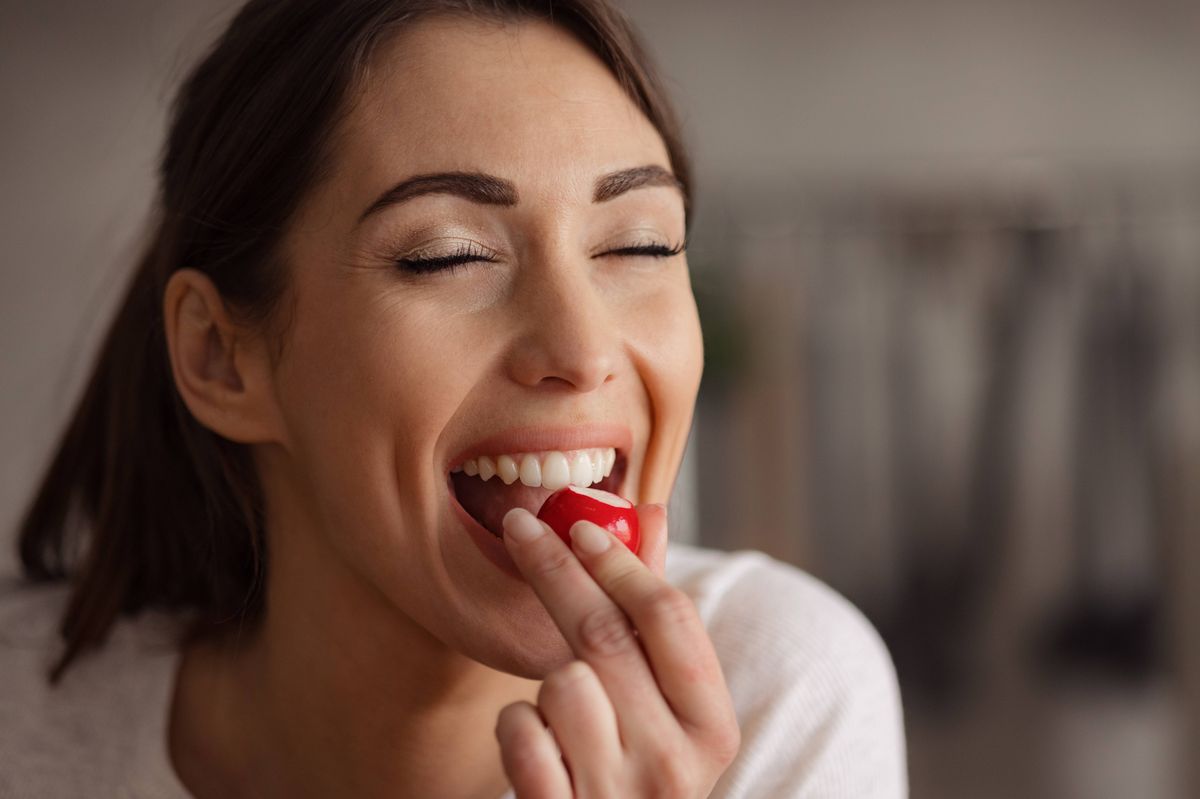 Portrait of happy woman enjoying while eating fresh radish with her eyes closed at home.